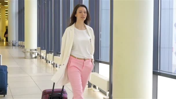 Tourist tjej med bagage i internationella flygplats går med hennes bagage. Flygbolaget passageraren i en flygplatslounge väntar flyg flygplan. Slow Motion — Stockvideo