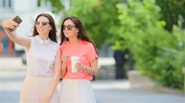 Selfie akıllı telefon ile açık havada alarak iki genç kız. Smartphone kullanarak kahve ile alışveriş sonra iki kadın