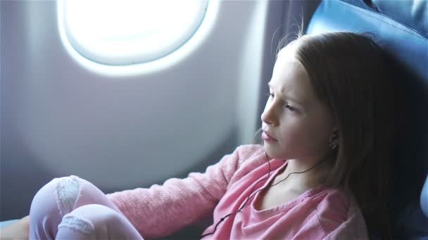 Очаровательная маленькая девочка путешествует на самолёте. Милый ребенок смотрит кино у окна в самолете. Медленное движение — стоковое видео