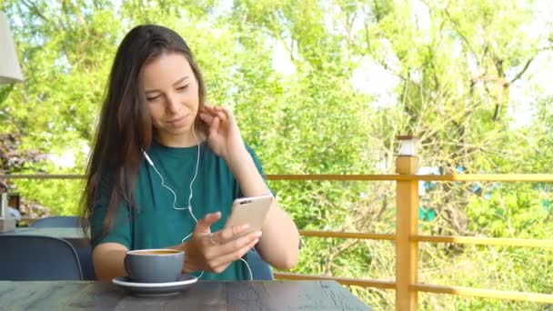 Mujer joven llamando con teléfono celular mientras está sentada sola en la cafetería durante el tiempo libre. Atractiva hembra con linda sonrisa teniendo conversación con el teléfono móvil mientras descansa en la cafetería — Vídeo de stock