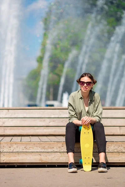Portrait of happy young urban girl with skateboard in european city. Caucasian tourist background the big fountain — Stock Photo, Image
