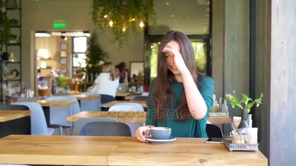 Молодая женщина, сидящая в кафе на открытом воздухе и пьющая кофе. Портрет счастливой девушки с чашкой кофе — стоковое видео
