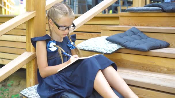 Imádnivaló kis iskola lány jegyzeteket és a ceruza szabadtéri. Vissza az iskolába. — Stock videók