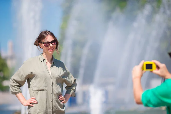 Ung man tar en bild av hans flickvän sitter bakgrund fontänen. Ung man gör foto av kvinna på den gatan skrattar och har kul i sommar. — Stockfoto