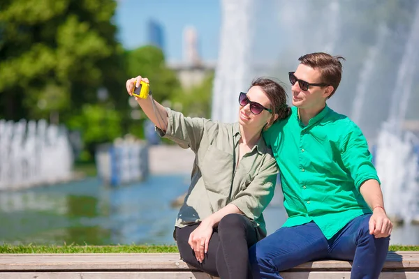 Pareja tomando un selfie fondo de la fuente. Joven hombre haciendo foto de mujer en la calle riendo y divirtiéndose en verano . — Foto de Stock
