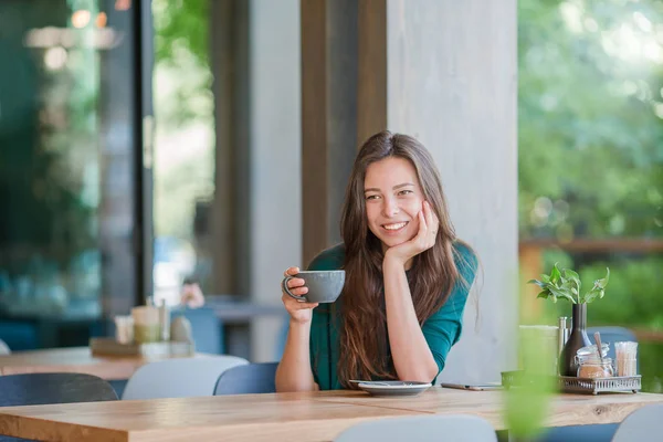 Красивая девушка с горячим кофе завтракает в кафе на открытом воздухе. Счастливая городская женщина пьет кофе — стоковое фото