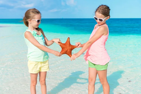 Adoráveis meninas se divertindo na praia cheia de estrelas do mar na areia — Fotografia de Stock