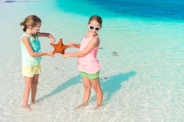 Adoráveis meninas se divertindo na praia cheia de estrelas do mar na areia — Fotografia de Stock