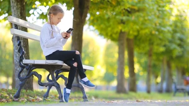 Lilla bedårande flickan med smartphone i höst. Kid har kul på varma soliga höstdag utomhus — Stockvideo