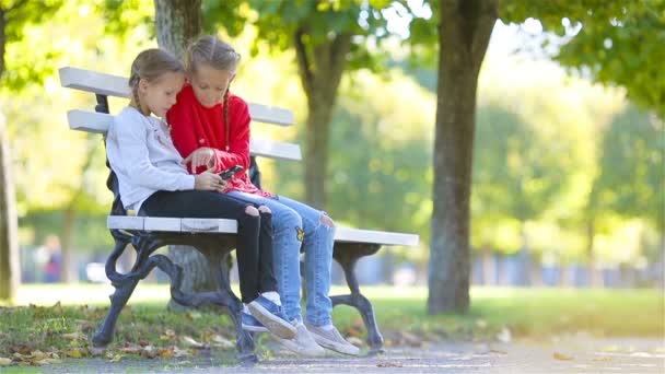 Niñas adorables con teléfono inteligente en otoño. Niños divirtiéndose en el cálido día soleado de otoño al aire libre — Vídeos de Stock