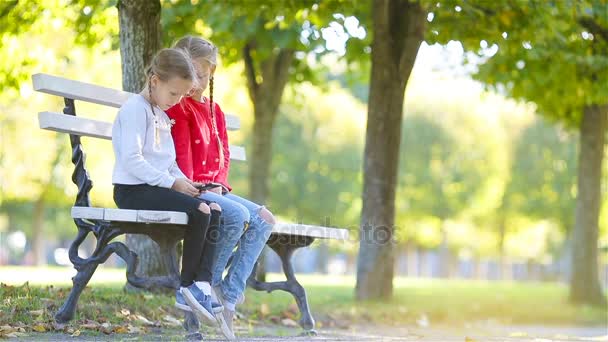 Little adorable girls with smartphone in fall outdoors. Kids having fun at warm sunny day in autumn park — Stock Video