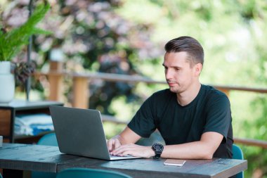 Dizüstü bilgisayar açık Cafe kahve içme ile genç adam. Hareket eden smartphone kullanan adam.