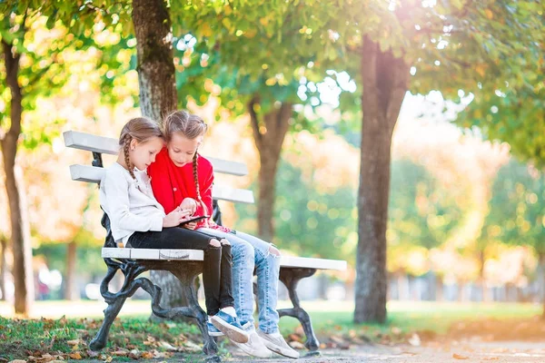 Pequenas garotas adoráveis com smartphone no outono ao ar livre. Crianças se divertindo no dia ensolarado quente no parque de outono — Fotografia de Stock