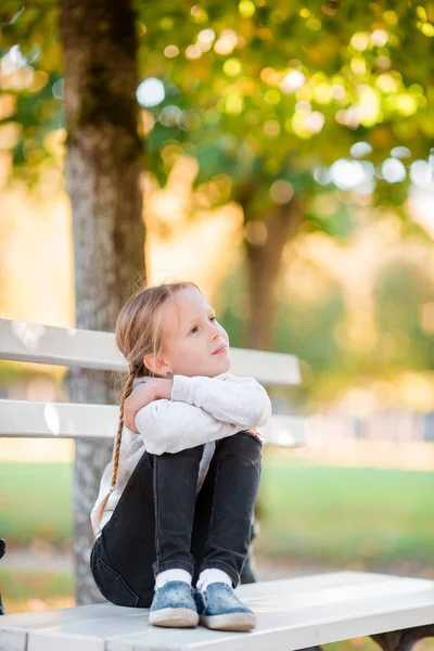 Adorable niña en el hermoso día de otoño al aire libre. Niña en el banco en otoño —  Fotos de Stock