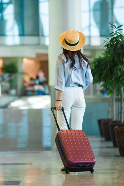 Giovane donna in cappello con bagaglio in aeroporto internazionale a piedi con i suoi bagagli. Passeggero di una compagnia aerea in una lounge dell'aeroporto in attesa di un aereo di volo — Foto Stock