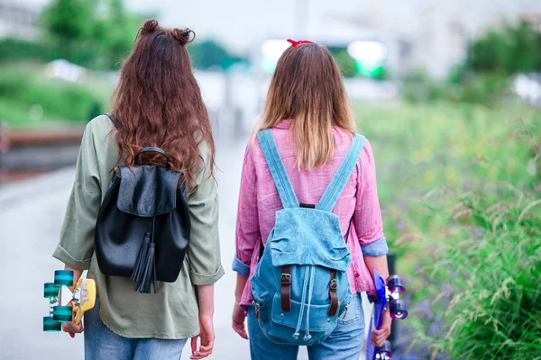 Gün batımı ışıkta açık havada kaykay ile iki hippi kız. Portre skatebords eller içinde. Aktif sportif kadınlara paten parkta birlikte eğleniyor.
