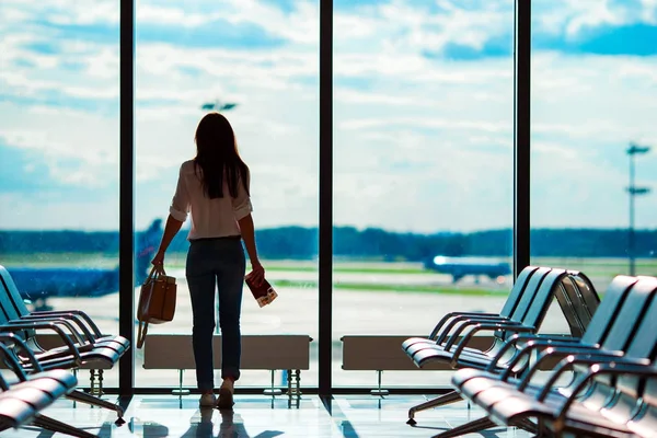Mujer joven en el aeropuerto internacional con su equipaje fondo ventana grande. Pasajero de aerolínea en un salón del aeropuerto esperando aviones de vuelo — Foto de Stock