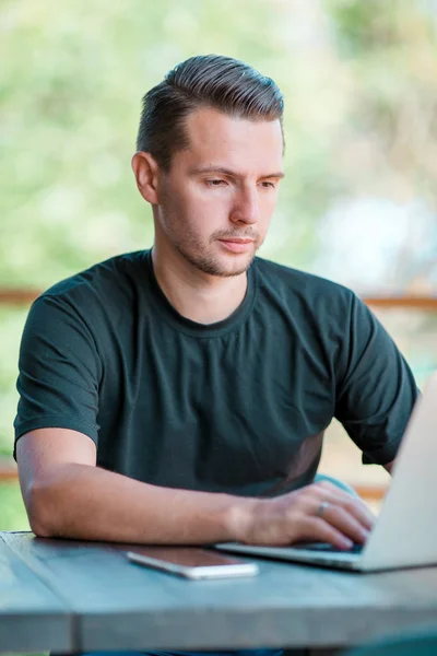 Jonge man met laptop in outdoor cafe koffie drinken. Man met mobiele smartphone. — Stockfoto