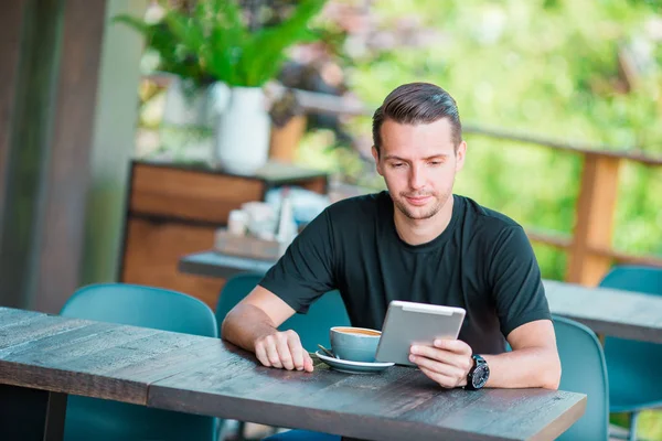 Jonge man met laptop in outdoor cafe koffie drinken. Man met mobiele smartphone. — Stockfoto