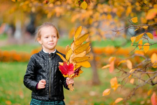 Portrait of adorable little girl with yellow leaves bouquet in fall on scooter — Stock Photo, Image