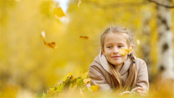 Портрет очаровательной маленькой девочки с желтыми листьями букет осенью. Красивый улыбающийся ребенок лежит на ковре из листьев — стоковое видео