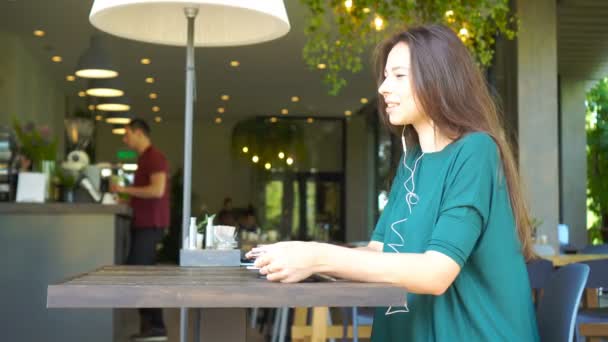 Mujer joven llamando por teléfono mientras está sentada sola en la cafetería durante el día de verano . — Vídeo de stock