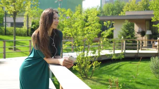 Mujer joven escuchando la música por los auriculares. Atractiva hembra con linda sonrisa con teléfono móvil mientras descansa en la cafetería — Vídeos de Stock