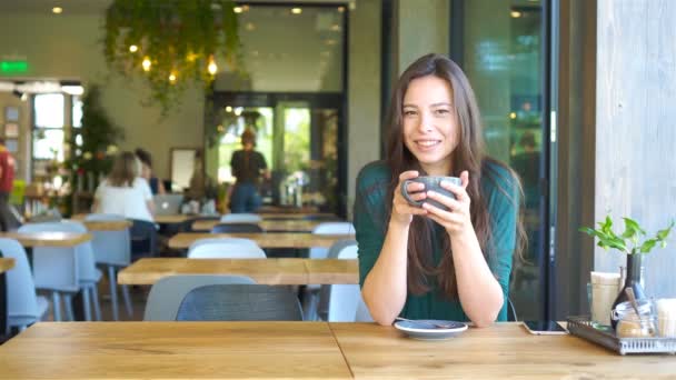 Mujer joven sentada en un café al aire libre bebiendo café. Retrato de chica feliz con taza de café — Vídeos de Stock