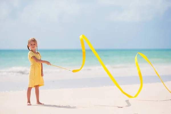 Adorable niña bailando con cinta de gimnasia amarilla en la playa —  Fotos de Stock