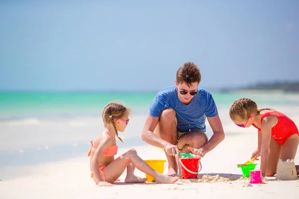 Vader en kinderen maken zandkasteel op tropisch strand. Familie spelen met strand speelgoed — Stockfoto