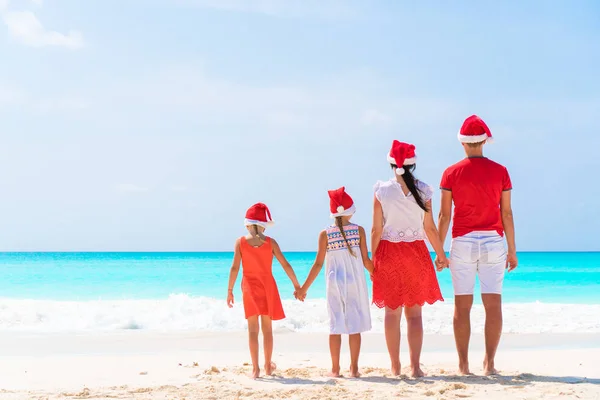 Happy rodinkou v červené Santa klobouky na tropické pláži slaví Vánoce — Stock fotografie