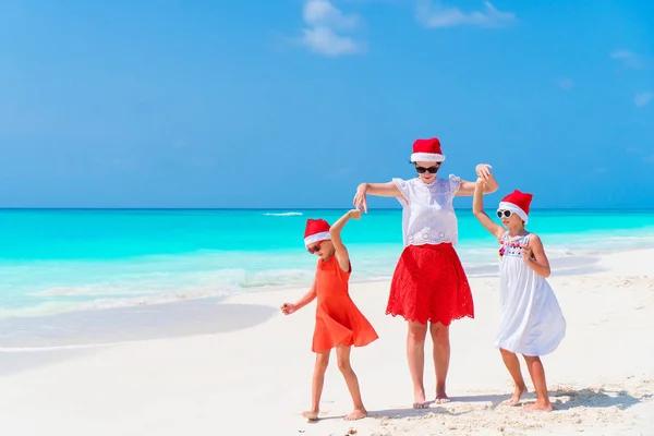 Happy beautiful family of mom and kids in red Santa hats on a tropical beach celebrating Christmas — Stock Photo, Image