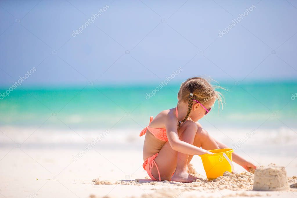 Little girl at tropical white beach making sand castle