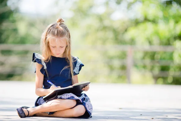 Bedårande liten skolflicka med anteckningar och pennor utomhus. Tillbaka till skolan. — Stockfoto