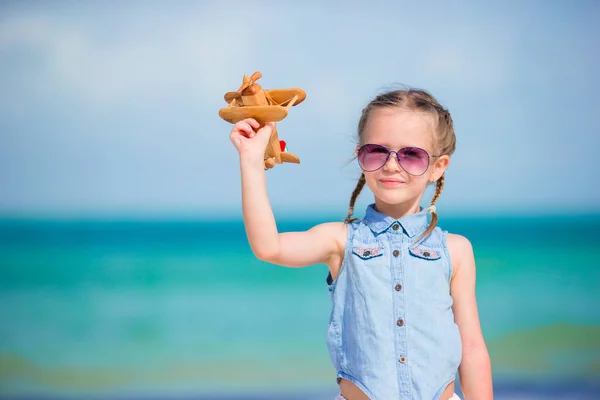 Glückliches kleines Mädchen mit Spielzeugflugzeug in der Hand am weißen Sandstrand — Stockfoto