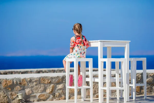 Adorable little girl having breakfast at outdoor cafe with sea view. Time for lunch. — Stock Photo, Image