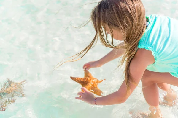 Adorable little girl with starfish on white empty beach — Stock Photo, Image