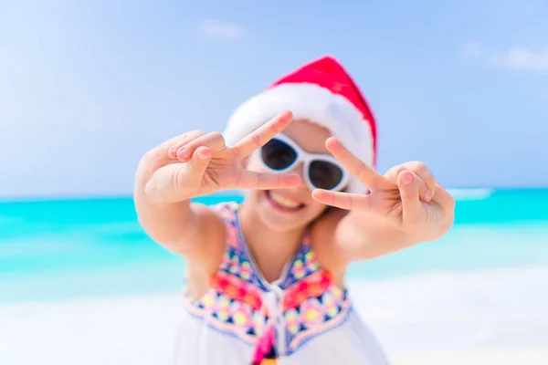 Entzückendes kleines Mädchen mit Weihnachtsmütze im Weihnachtsurlaub am Strand. Kleines Kind im Weihnachtsurlaub am Strand — Stockfoto