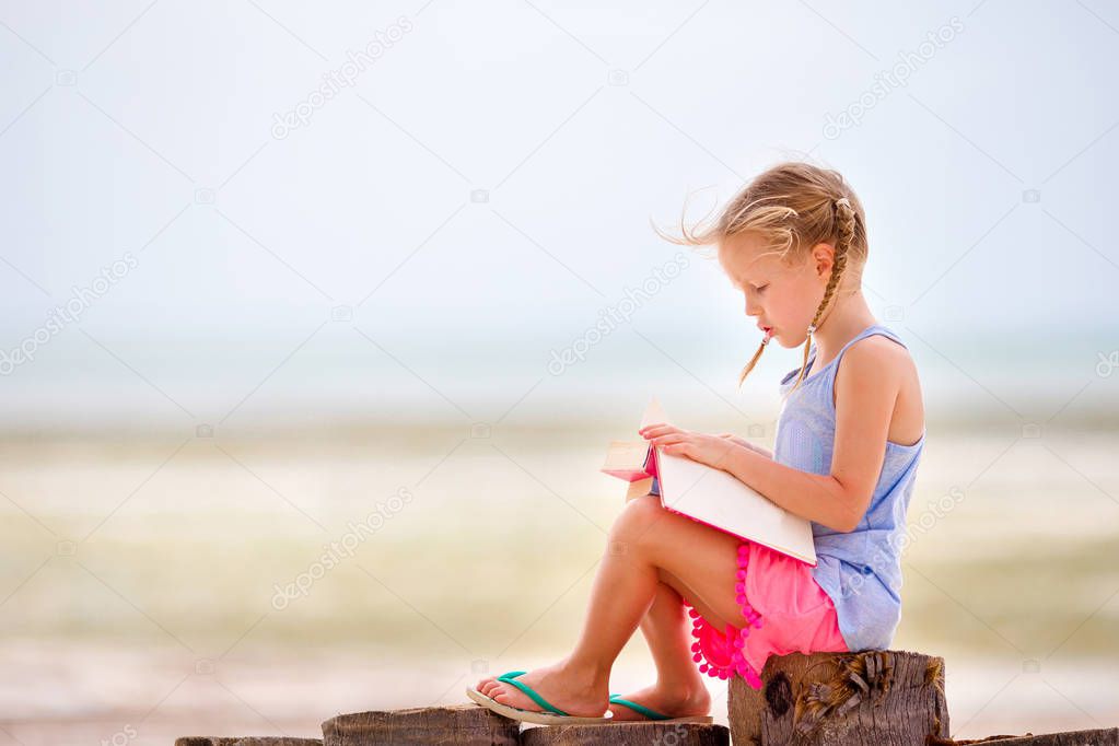 Little adorable girl reading book during tropical white beach