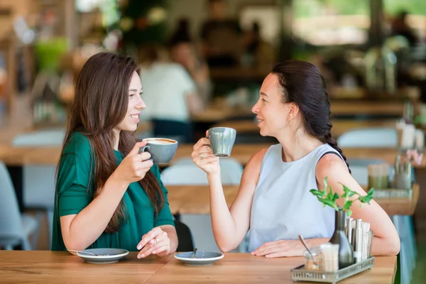 Счастливые молодые женщины с чашками кофе на открытом воздухе кафе. Концепция общения и дружбы — стоковое фото