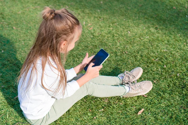 Bedårande liten flicka med telefon under sommaren semester utomhus — Stockfoto