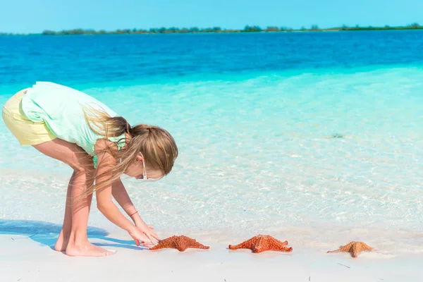 Adorable little girl with wild red starfish on white empty beach — Stock Photo, Image