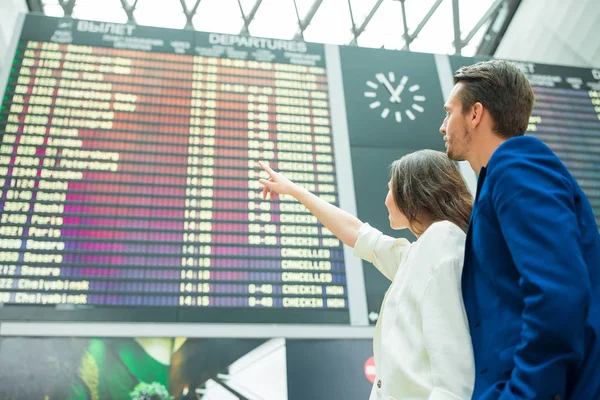 Jovem casal no aeroporto internacional olhando para a placa de informações de voo — Fotografia de Stock