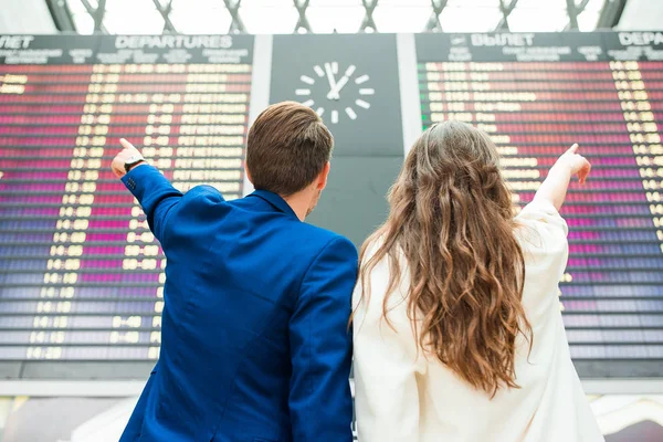 国際空港の若いカップルがフライト情報ボードを見て — ストック写真