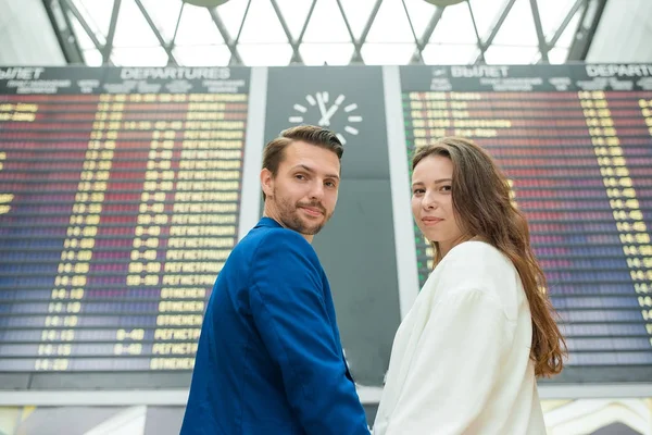 国際空港の若いカップルがフライト情報ボードを見て — ストック写真