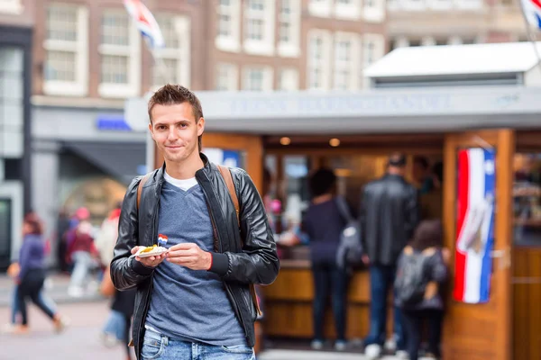 Vrolijke Kaukasische toerist met verse haring met uien- en nederlandse vlag in Amsterdam. Traditioneel Hollands eten buiten — Stockfoto