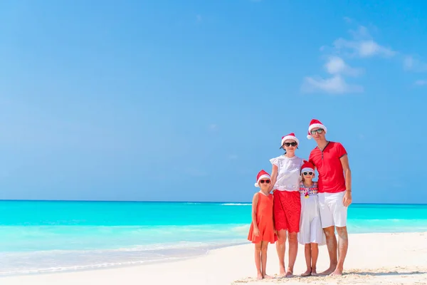 Happy family in red Santa hats on a tropical beach celebrating Christmas vacation — Stock Photo, Image