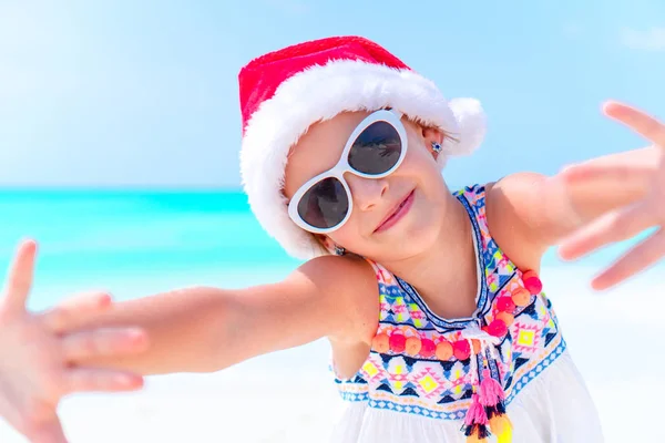 Urocza dziewczynka w kapeluszu Santa podczas świąt Bożego Narodzenia na plaży — Zdjęcie stockowe