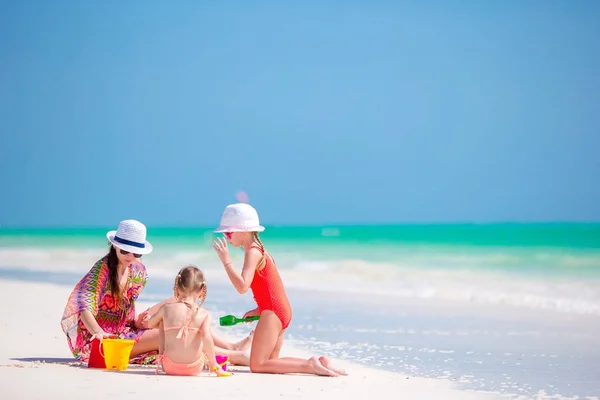 Anne ve küçük kızları tropik sahilde kumdan kale yapıyorlar. — Stok fotoğraf