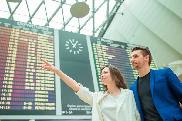 Joven hombre y mujer en el aeropuerto internacional mirando el tablero de información de vuelo — Foto de Stock